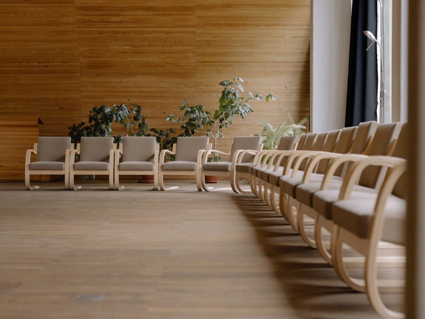 Salle d'attente claire aux fauteuils alignés sur un parquet, plantes au fond