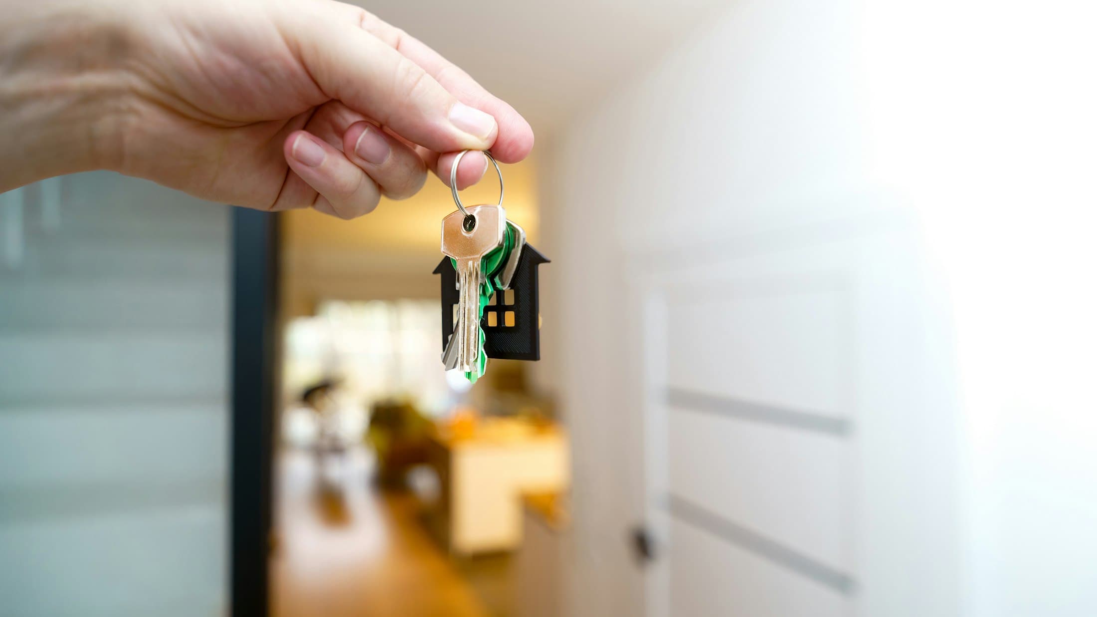 Main qui tend un trousseau de clés devant l’entrée d’un logement