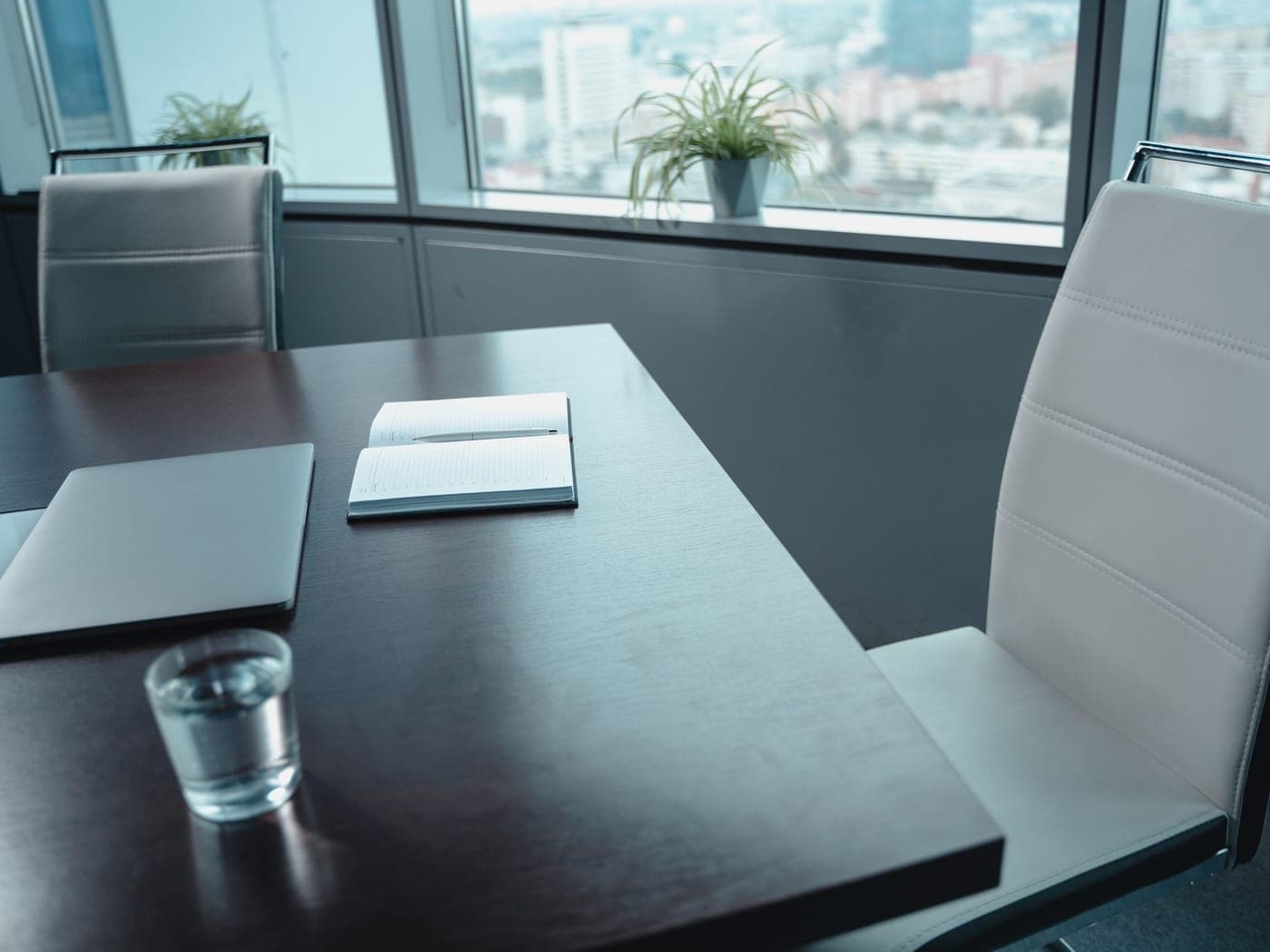 Table de bureau dégagée près d'une grande baie vitrée, verre d'eau et carnet