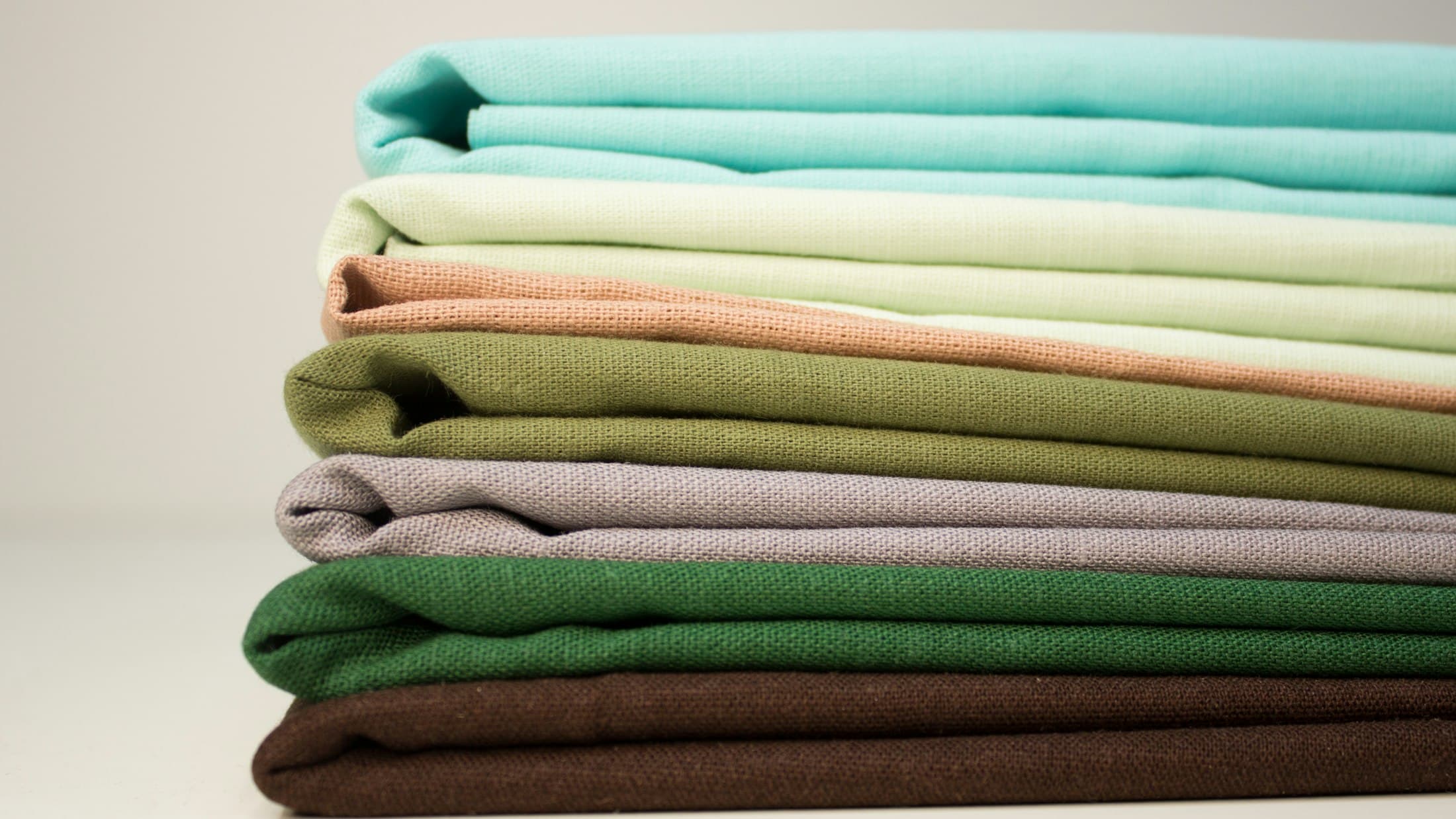 Pile de linge de maison repassé et plié, dans des tons verts et bleus